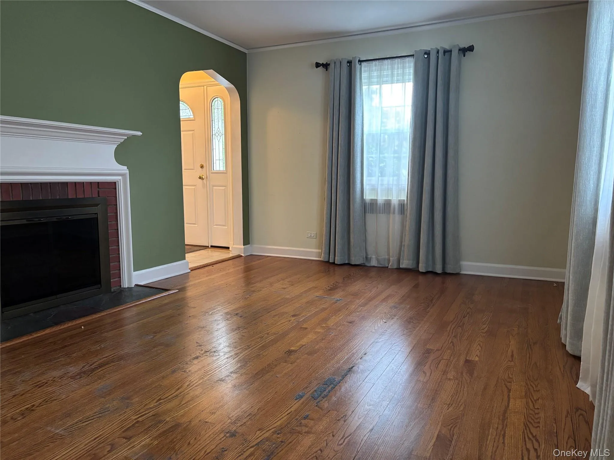 Living area featuring hardwood flooring, a fireplace with a white mantel and brick surround, and an arched entry Living area featuring hardwood flooring, a fireplace with a white mantel and brick surround, and an arched entry