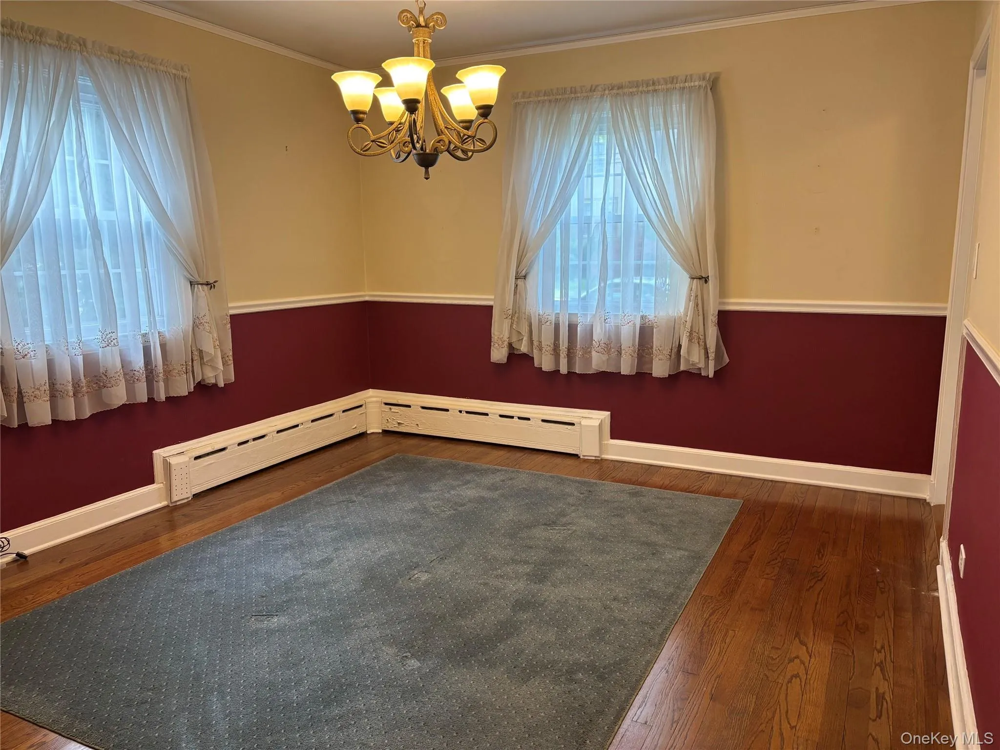 Interior room featuring wood-finish flooring, a decorative chandelier, and a window with sheer curtains Interior room featuring wood-finish flooring, a decorative chandelier, and a window with sheer curtains