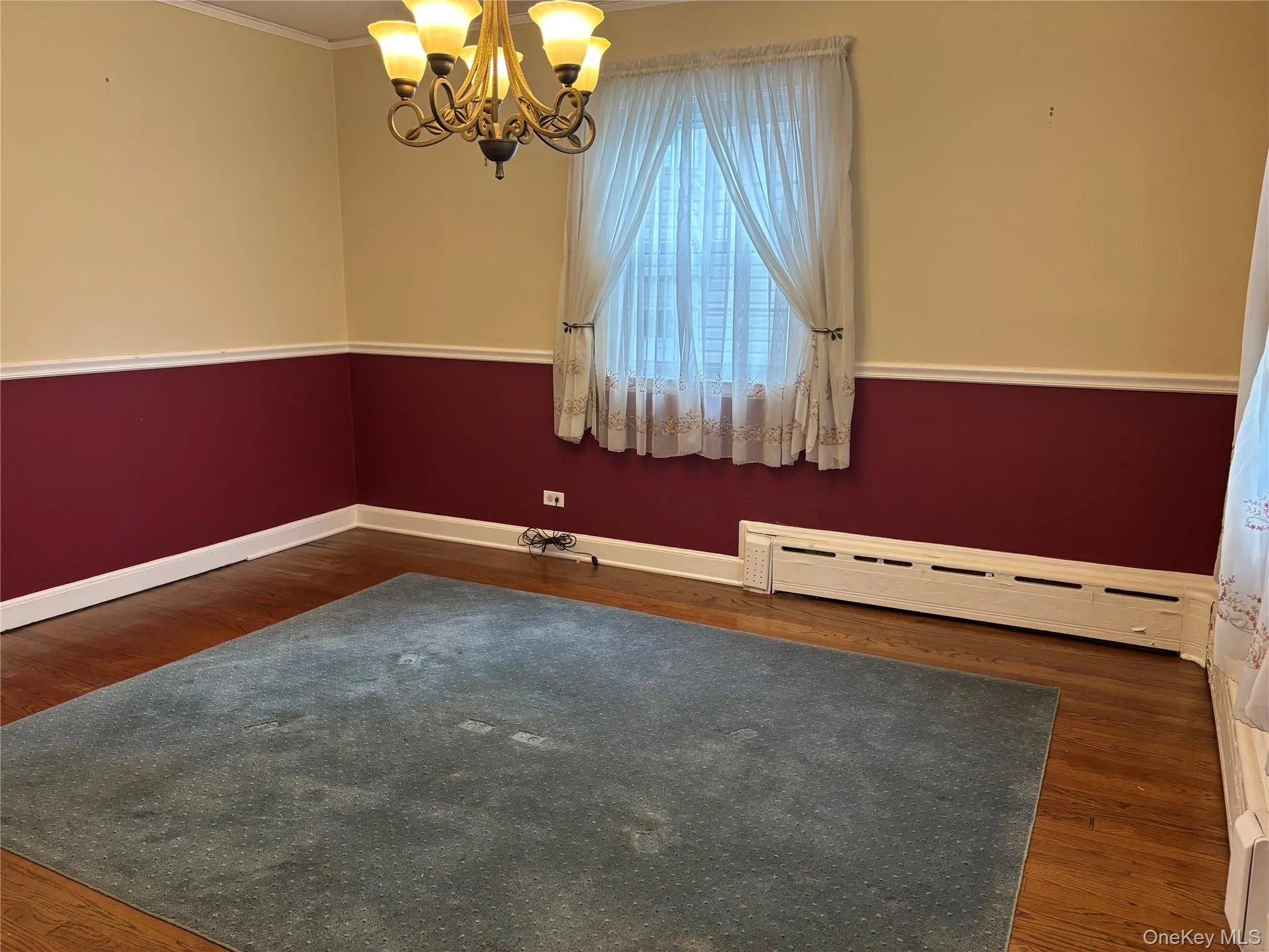 Interior room featuring wood-finish flooring, a decorative chandelier, and a window with sheer curtains Interior room featuring wood-finish flooring, a decorative chandelier, and a window with sheer curtains