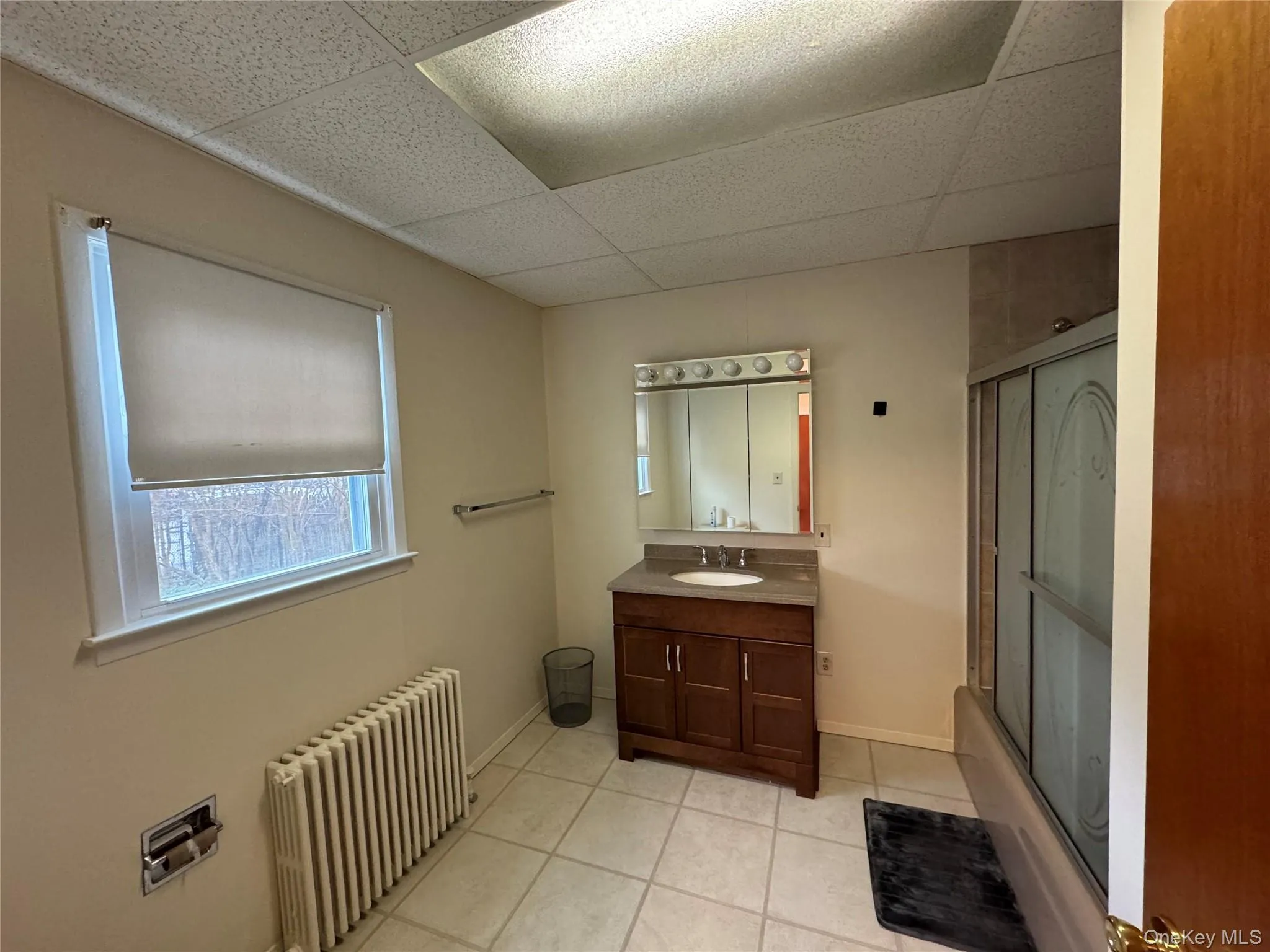 Bathroom featuring ceramic tile flooring, a wood-finish vanity with an integrated sink, a mirrored medicine cabinet, and a shower with frosted glass doors Bathroom featuring ceramic tile flooring, a wood-finish vanity with an integrated sink, a mirrored medicine cabinet, and a shower with frosted glass doors