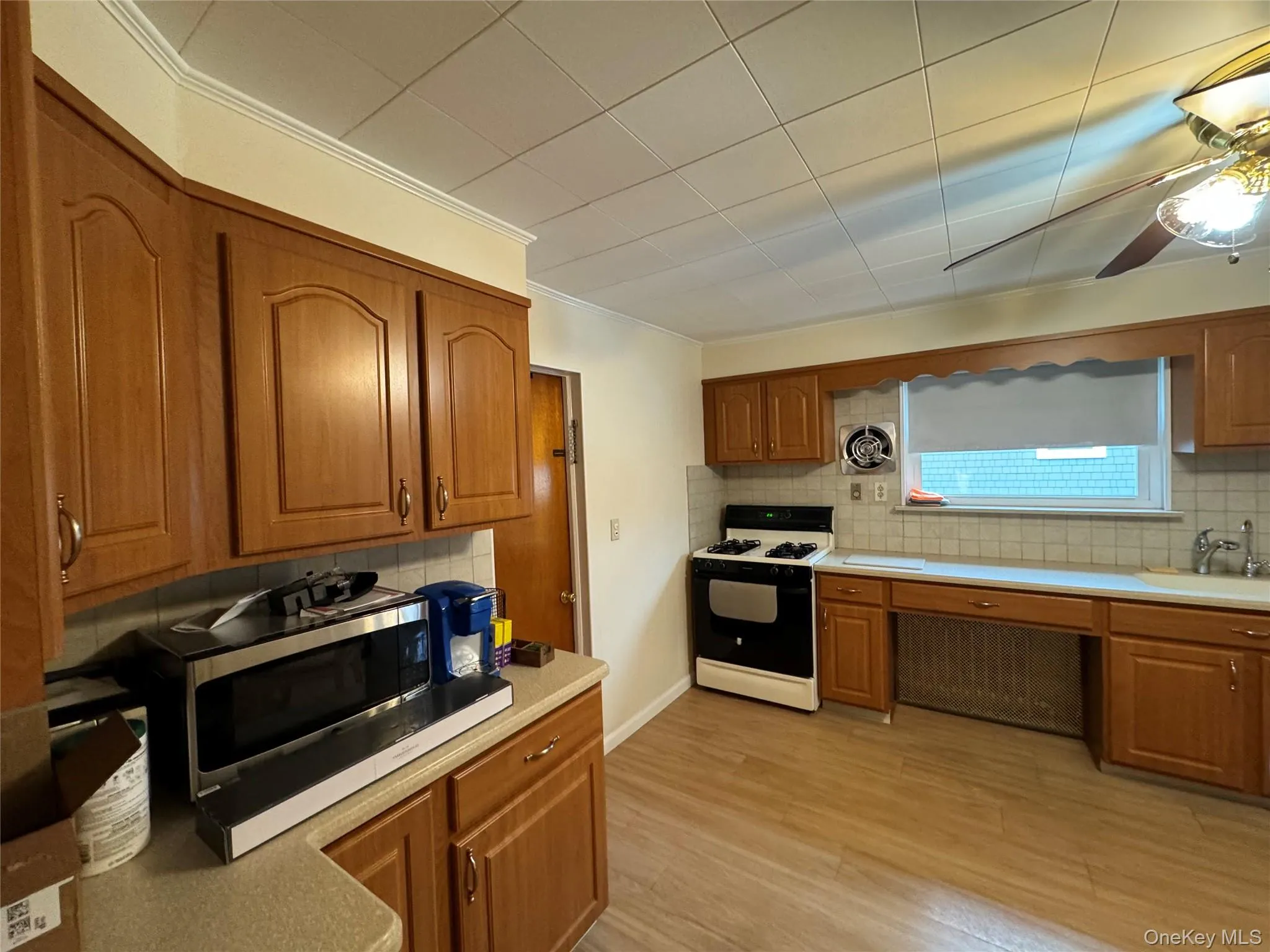 Kitchen featuring wood-finish cabinetry, tile backsplash, laminate countertops, and wood-look flooring Kitchen featuring wood-finish cabinetry, tile backsplash, laminate countertops, and wood-look flooring
