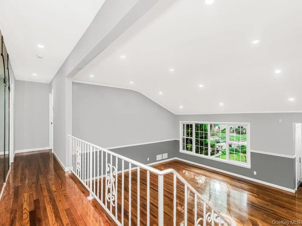 Open-concept living space with dark wood-finish flooring, recessed lighting, white wall trim, and a decorative railing Open-concept living space with dark wood-finish flooring, recessed lighting, white wall trim, and a decorative railing