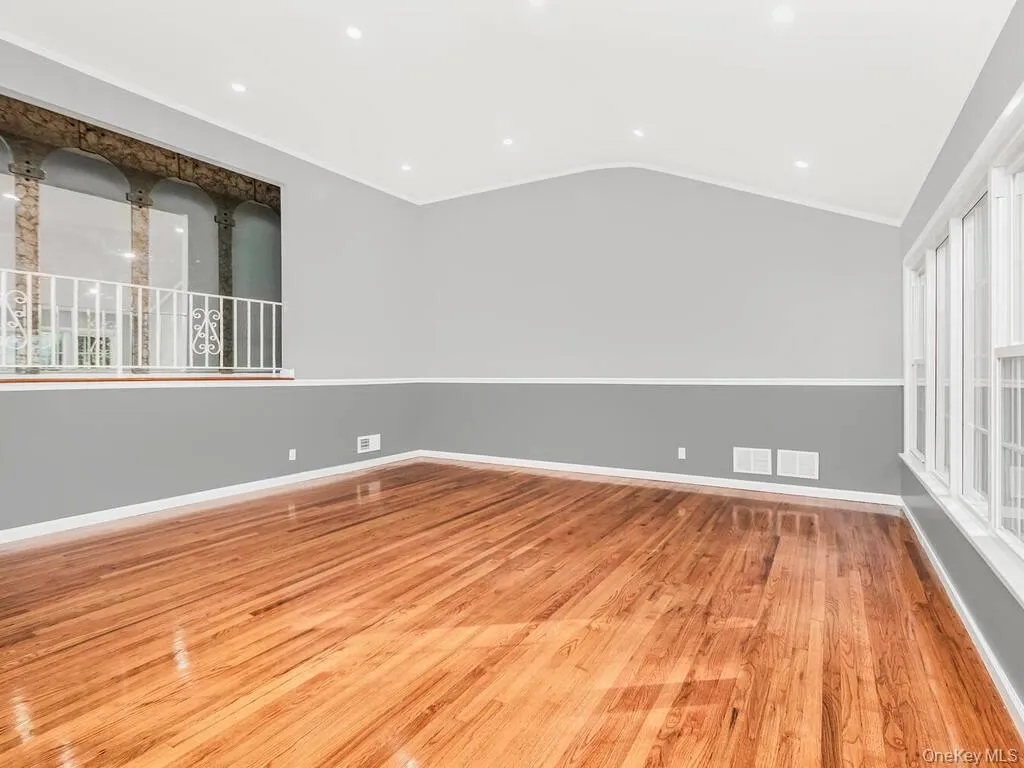 Spacious interior featuring wood-finish flooring, a vaulted ceiling with recessed lighting, and a partial decorative balcony with white railing Spacious interior featuring wood-finish flooring, a vaulted ceiling with recessed lighting, and a partial decorative balcony with white railing