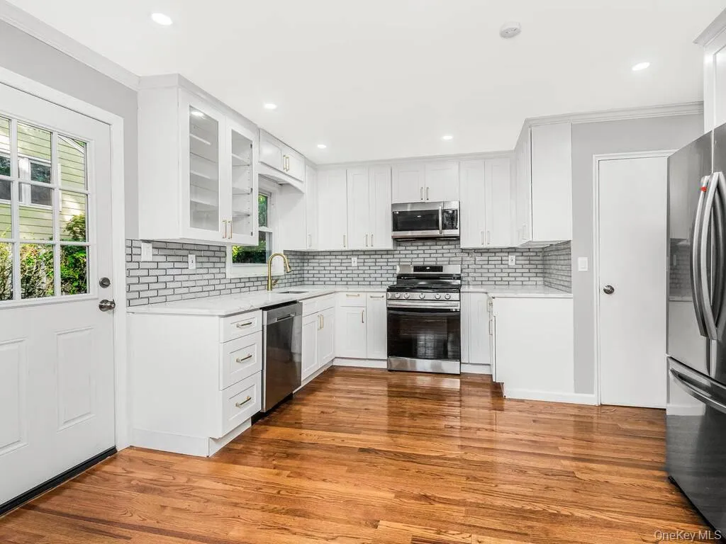 Modern kitchen featuring wood-finish flooring, white cabinetry, a subway tile backsplash, stainless steel appliances, and a glass-paneled exterior door Modern kitchen featuring wood-finish flooring, white cabinetry, a subway tile backsplash, stainless steel appliances, and a glass-paneled exterior door