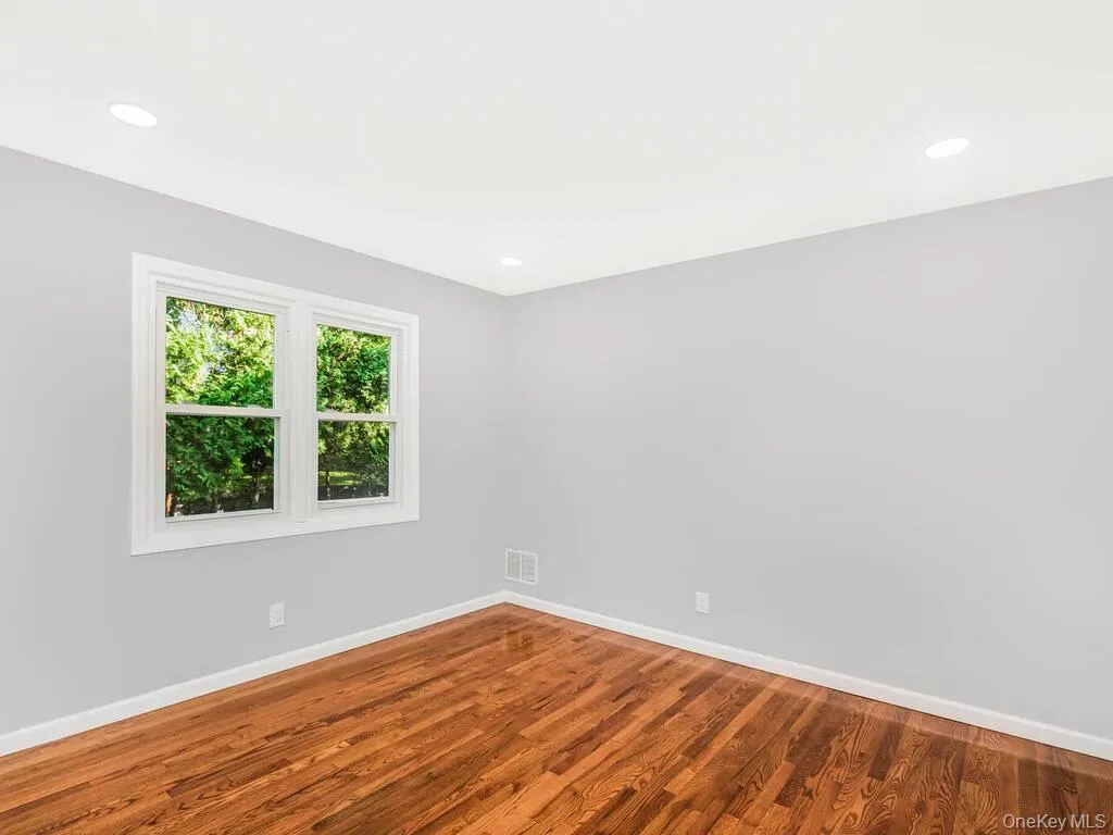 Inviting interior space featuring rich wood flooring, crisp white baseboards, and a large window with white trim Inviting interior space featuring rich wood flooring, crisp white baseboards, and a large window with white trim