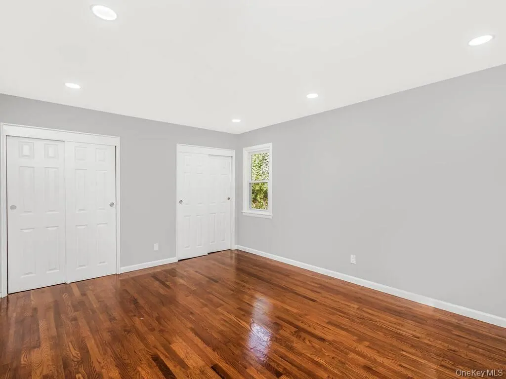 Spacious room featuring rich wood-finish flooring, recessed lighting, and two sets of sliding closet doors Spacious room featuring rich wood-finish flooring, recessed lighting, and two sets of sliding closet doors
