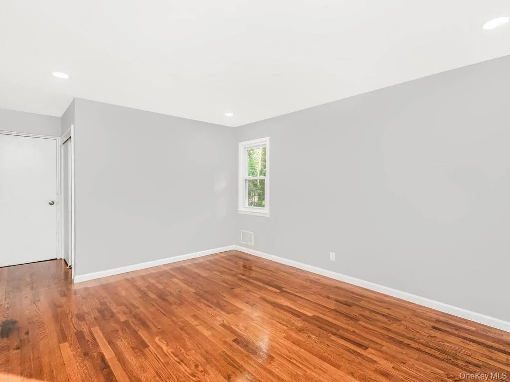 Room featuring wood-finish flooring, light grey walls, white trim, recessed lighting, and a window with white casing Room featuring wood-finish flooring, light grey walls, white trim, recessed lighting, and a window with white casing