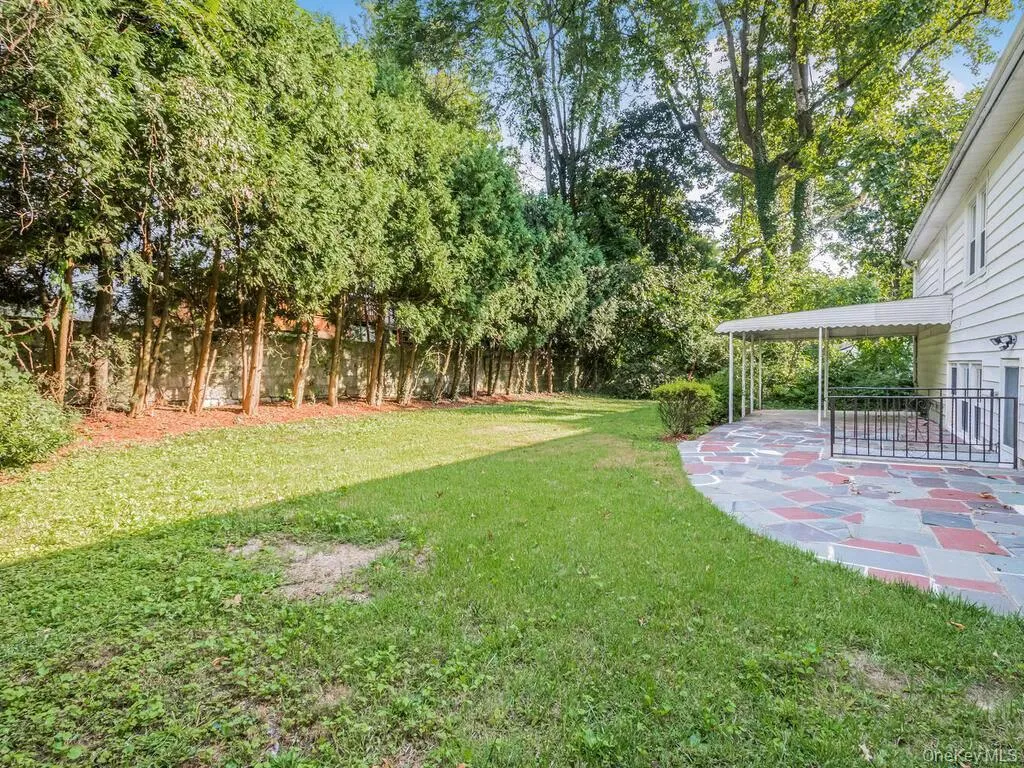 Expansive backyard featuring a curved flagstone patio, a covered patio area, and a large grassy expanse bordered by mature trees and a privacy fence Expansive backyard featuring a curved flagstone patio, a covered patio area, and a large grassy expanse bordered by mature trees and a privacy fence