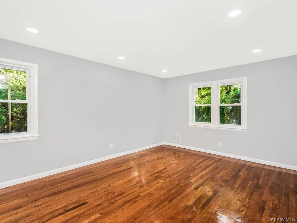 Hardwood flooring and recessed lighting illuminate this bright room featuring two large windows with white trim Hardwood flooring and recessed lighting illuminate this bright room featuring two large windows with white trim