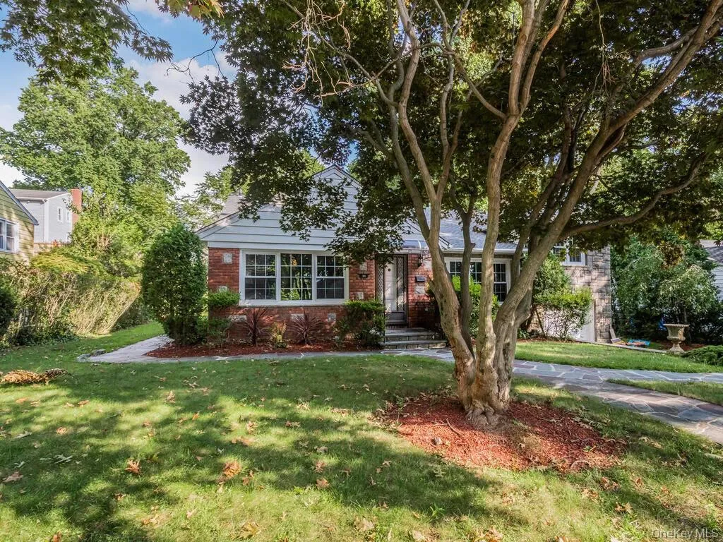 Brick and siding exterior featuring multiple paned windows, mature trees, a stone pathway, and a well-maintained lawn Brick and siding exterior featuring multiple paned windows, mature trees, a stone pathway, and a well-maintained lawn