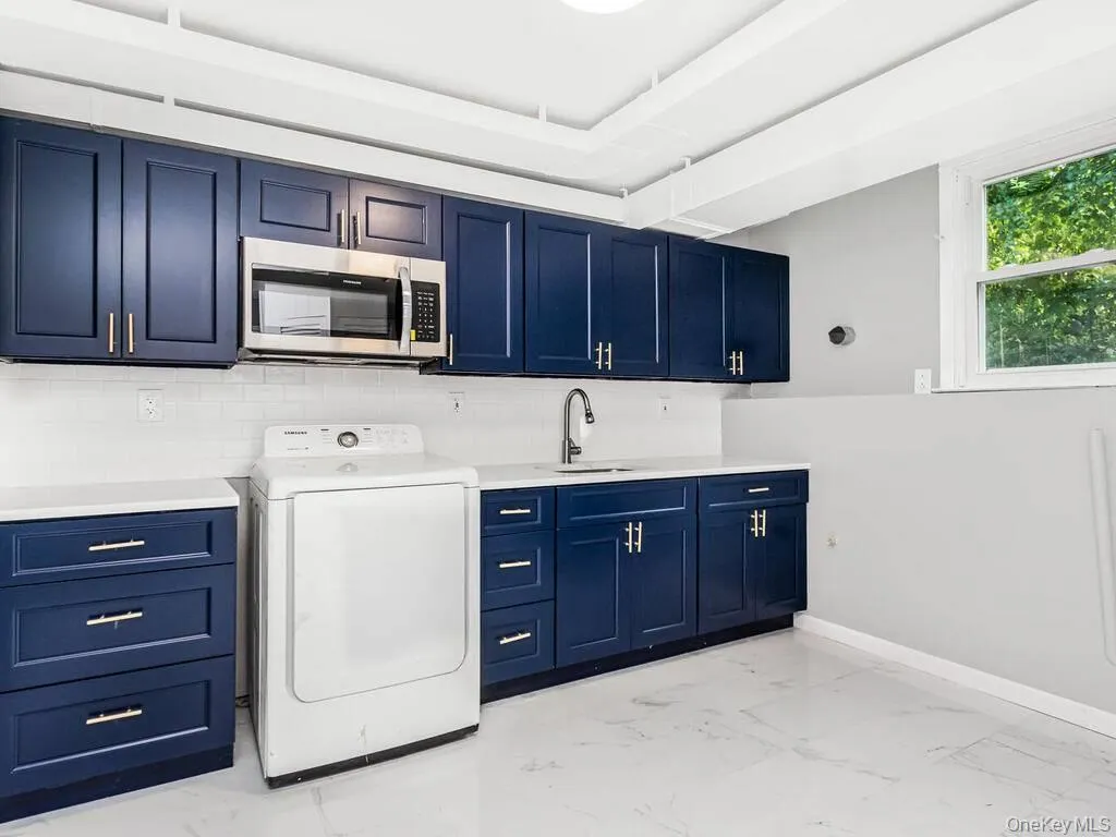 Laundry area featuring blue shaker-style cabinetry with silver hardware, white subway tile backsplash, and white countertops Laundry area featuring blue shaker-style cabinetry with silver hardware, white subway tile backsplash, and white countertops