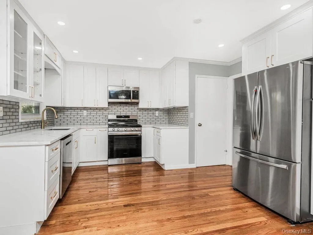 Renovated kitchen featuring white cabinetry, light-toned countertops, and a subway tile backsplash Renovated kitchen featuring white cabinetry, light-toned countertops, and a subway tile backsplash