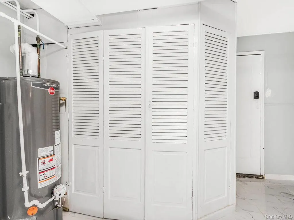 Utility closet with louvered bifold doors, featuring a water heater and visible plumbing Utility closet with louvered bifold doors, featuring a water heater and visible plumbing