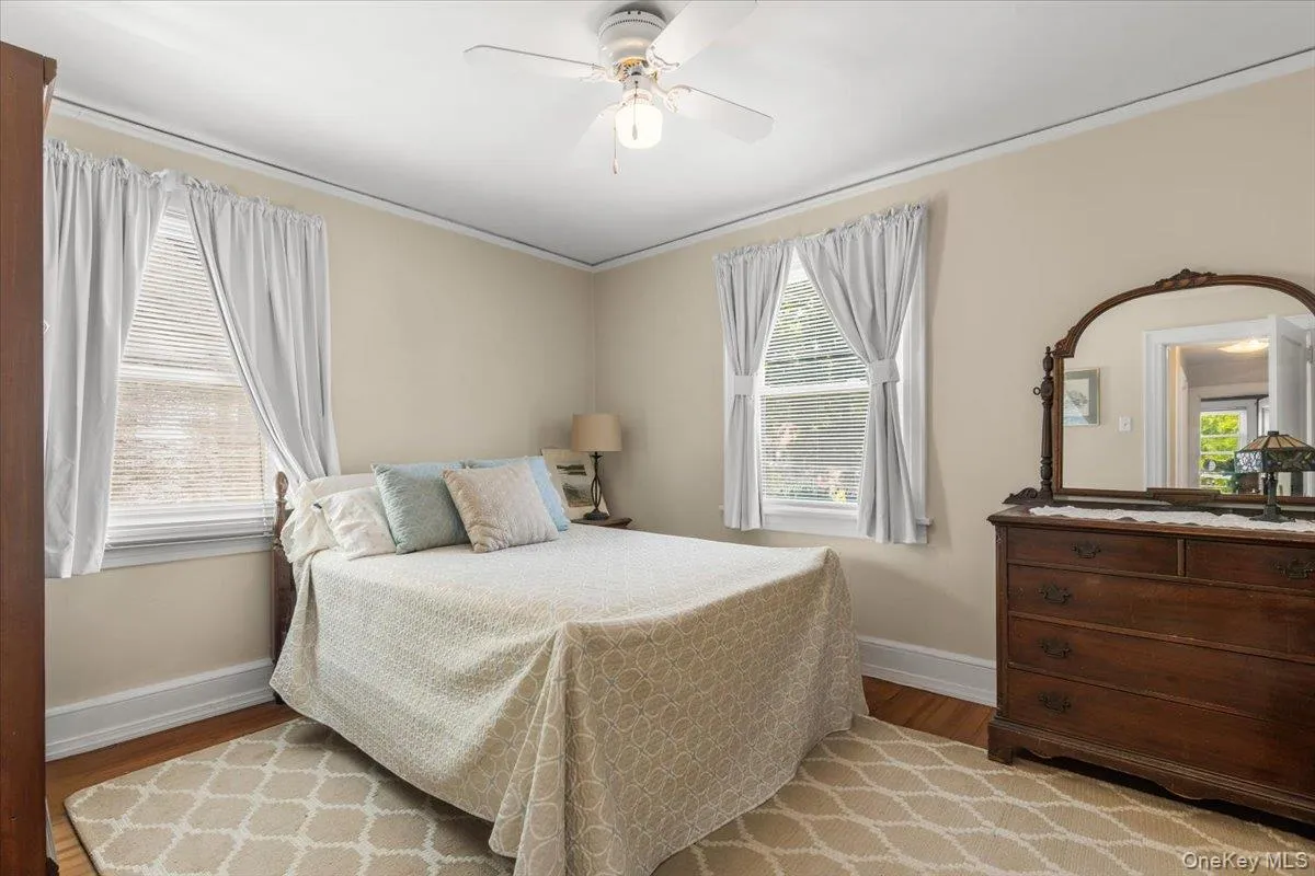 Room featuring wood-finish flooring, two double-hung windows with blinds, a ceiling fan with integrated lighting, and crown molding Room featuring wood-finish flooring, two double-hung windows with blinds, a ceiling fan with integrated lighting, and crown molding