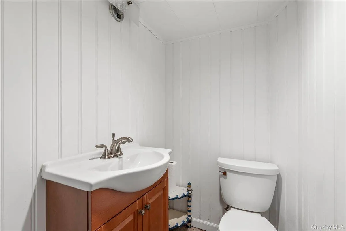 Pedestal sink with a cherry wood-finish vanity, brushed nickel faucet, and beadboard wall paneling Pedestal sink with a cherry wood-finish vanity, brushed nickel faucet, and beadboard wall paneling