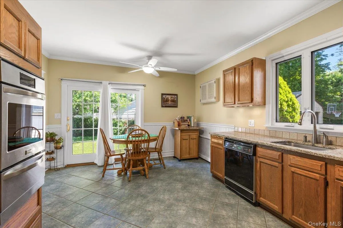 Kitchen featuring tiled flooring, a double oven, light wood-finish cabinetry, stone-finish countertops, and a stainless steel sink with an integrated dishwasher Kitchen featuring tiled flooring, a double oven, light wood-finish cabinetry, stone-finish countertops, and a stainless steel sink with an integrated dishwasher