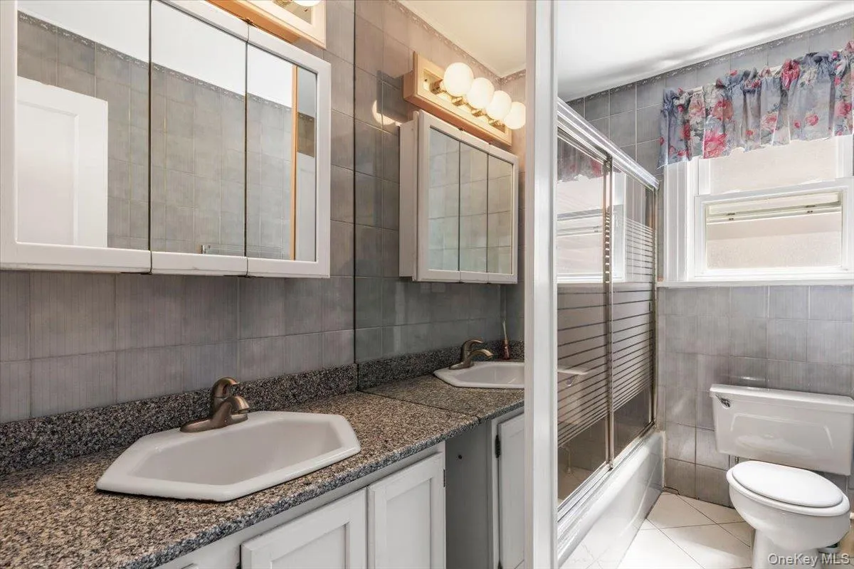 Bathroom with dual sinks, a granite-finish countertop, and white cabinetry Bathroom with dual sinks, a granite-finish countertop, and white cabinetry