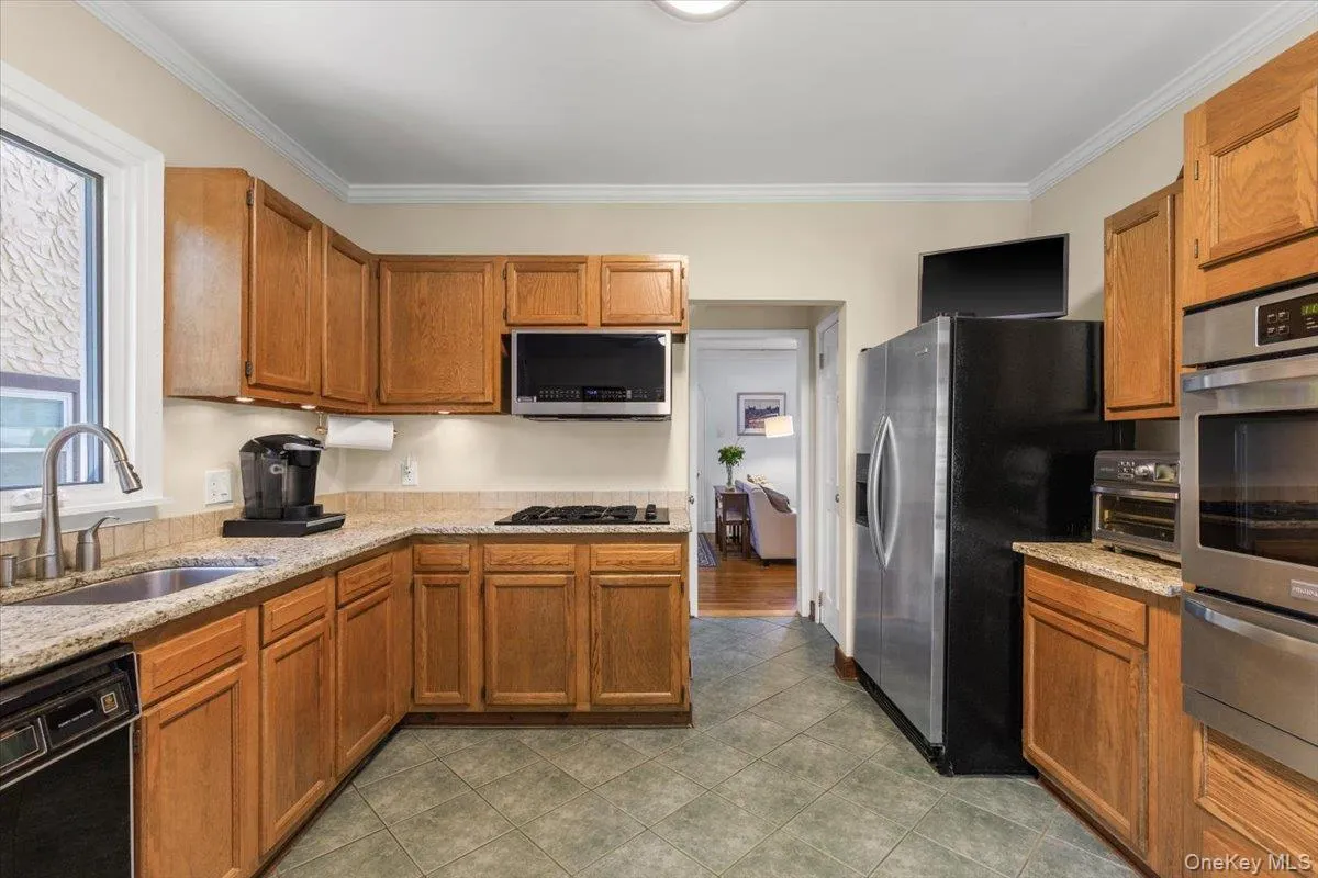 Kitchen featuring wood cabinetry, granite countertops, tile flooring, and stainless steel appliances Kitchen featuring wood cabinetry, granite countertops, tile flooring, and stainless steel appliances