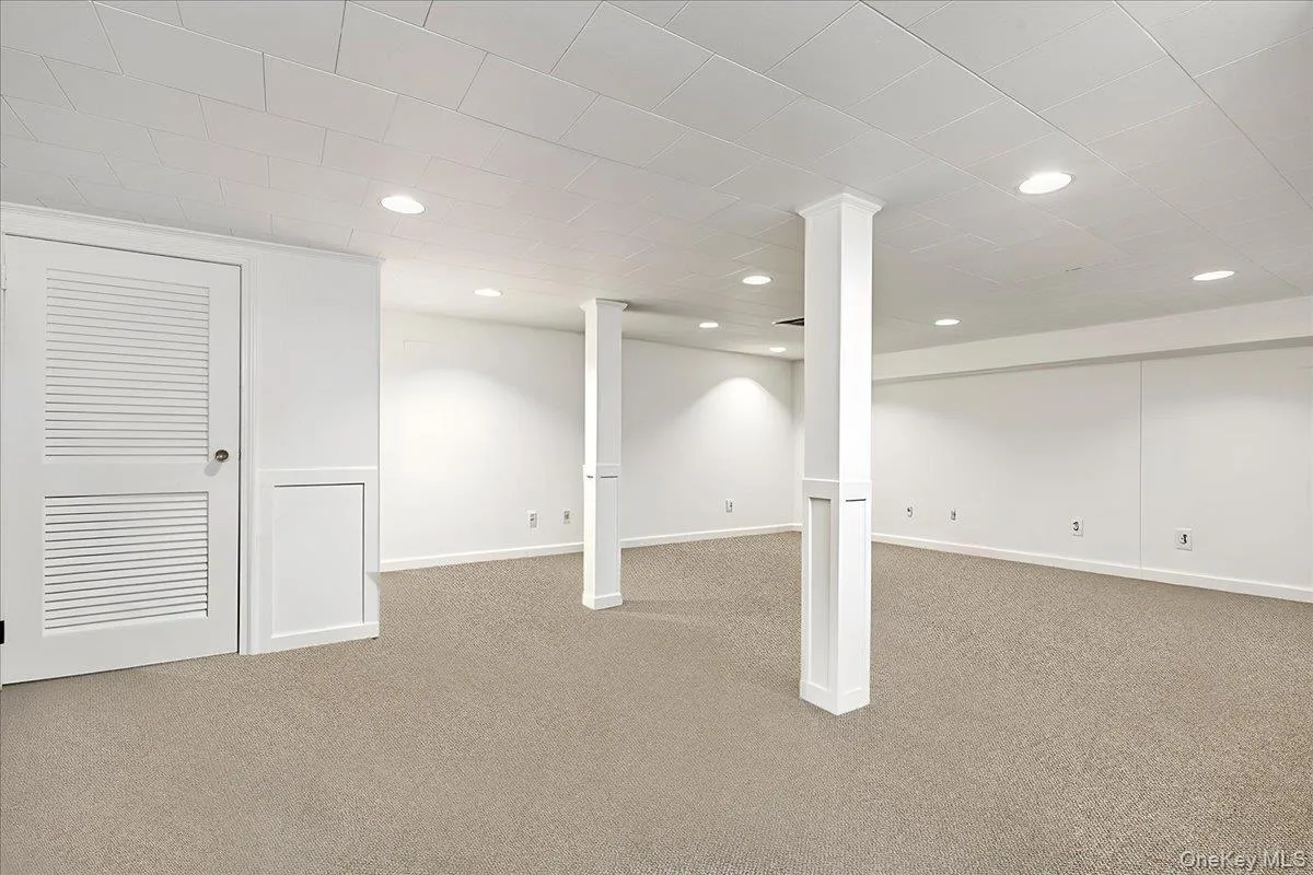 Spacious finished room featuring neutral carpet flooring, recessed lighting, white walls, decorative support columns, and a louvered door Spacious finished room featuring neutral carpet flooring, recessed lighting, white walls, decorative support columns, and a louvered door