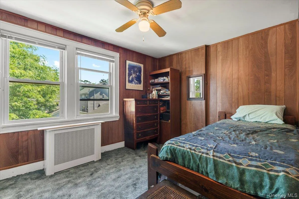 Interior room featuring wood paneling on walls, white trim around windows, and a white ceiling with a ceiling fan Interior room featuring wood paneling on walls, white trim around windows, and a white ceiling with a ceiling fan