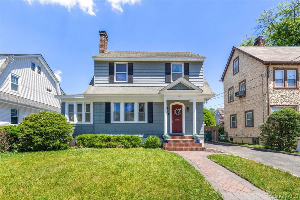 Two-story residence featuring light blue siding with dark shutters, a red entry door, and a brick pathway Two-story residence featuring light blue siding with dark shutters, a red entry door, and a brick pathway