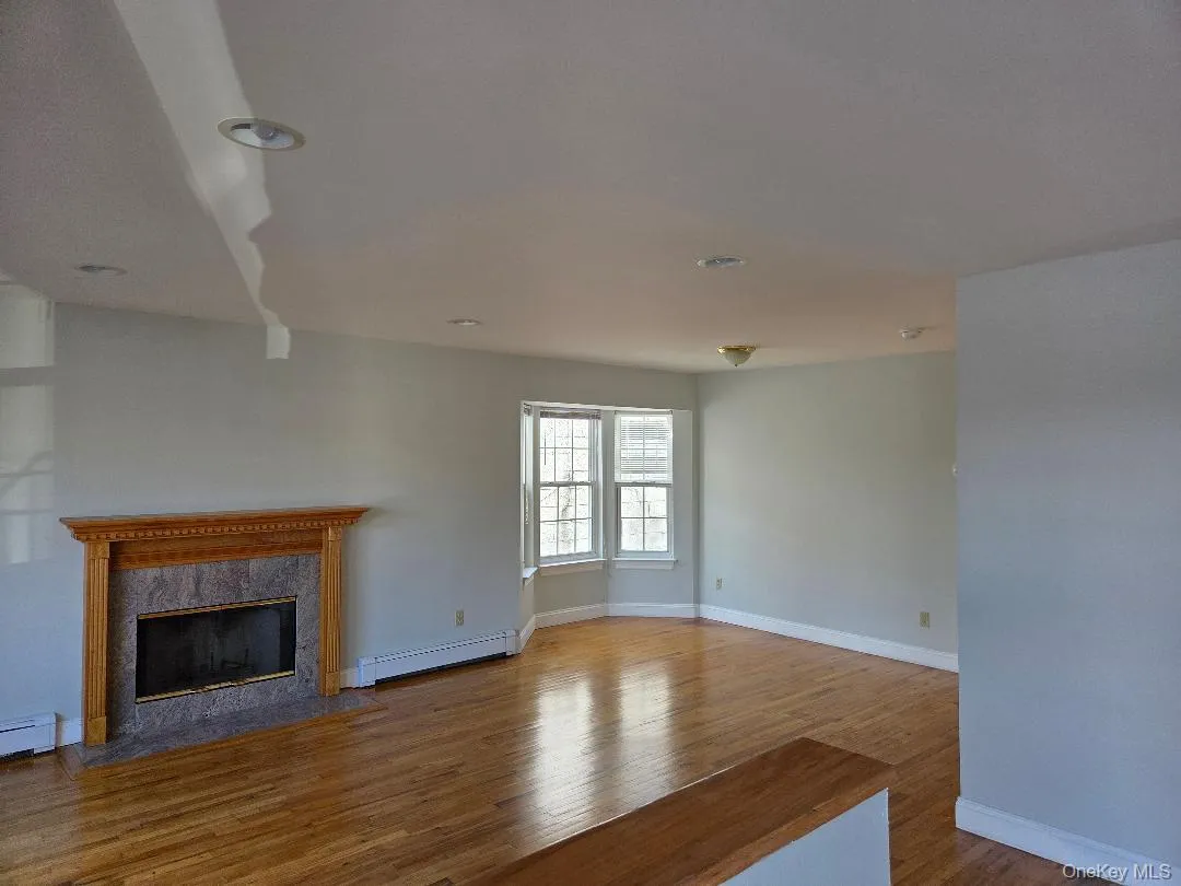 Unfurnished living room featuring a baseboard heating unit, baseboards, a premium fireplace, and wood finished floors Unfurnished living room featuring a baseboard heating unit, baseboards, a premium fireplace, and wood finished floors