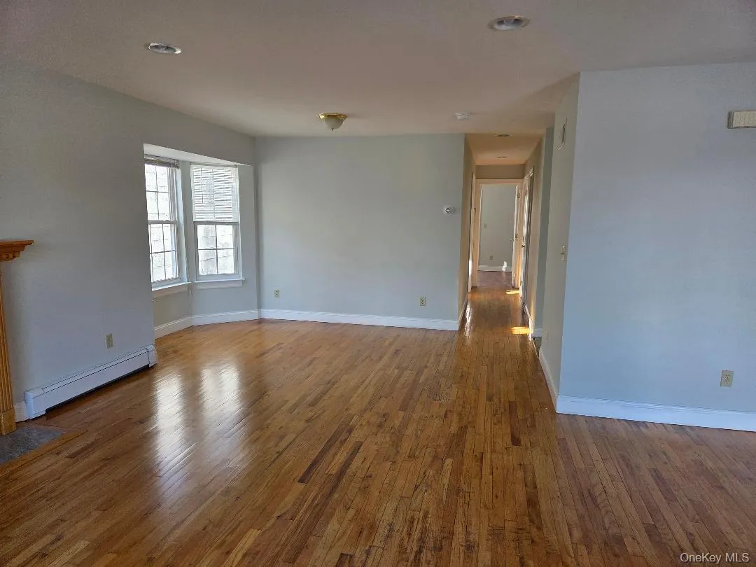 Unfurnished living room with a baseboard heating unit, baseboards, and wood finished floors Unfurnished living room with a baseboard heating unit, baseboards, and wood finished floors