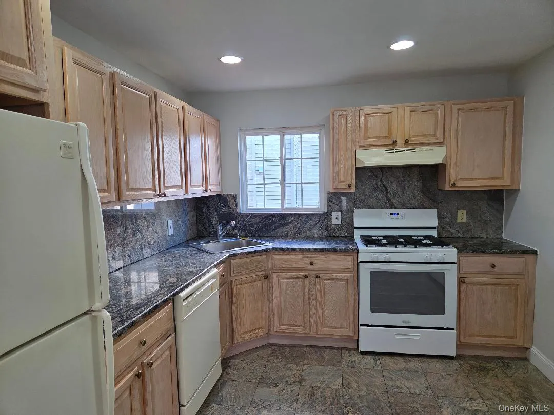 Kitchen featuring decorative backsplash, light brown cabinets, a sink, white appliances, and under cabinet range hood Kitchen featuring decorative backsplash, light brown cabinets, a sink, white appliances, and under cabinet range hood