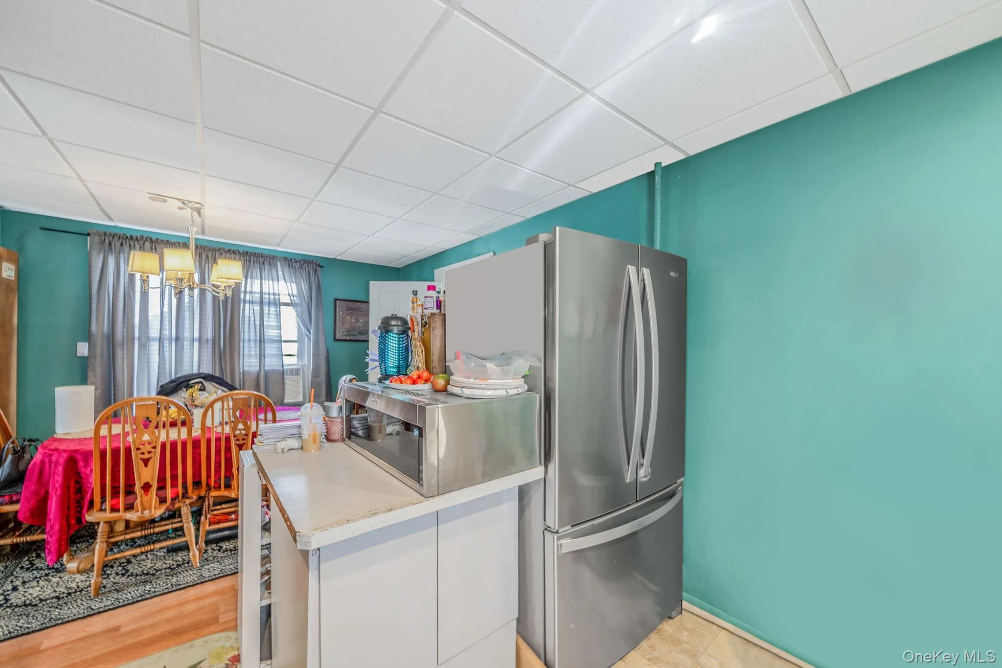 Kitchen featuring a chandelier, a drop ceiling, hanging light fixtures, freestanding refrigerator, and white cabinetry Kitchen featuring a chandelier, a drop ceiling, hanging light fixtures, freestanding refrigerator, and white cabinetry