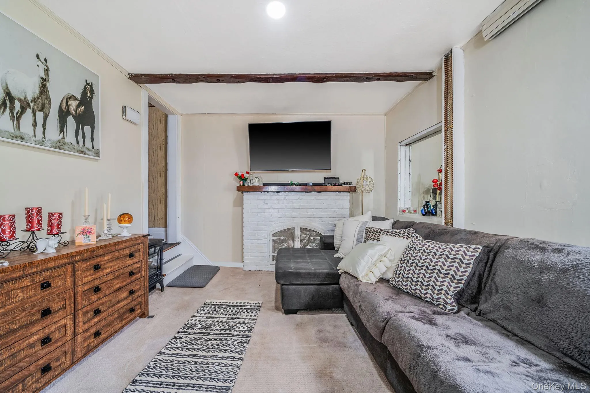 Carpeted living area featuring a fireplace, beamed ceiling, and a wall mounted air conditioner Carpeted living area featuring a fireplace, beamed ceiling, and a wall mounted air conditioner