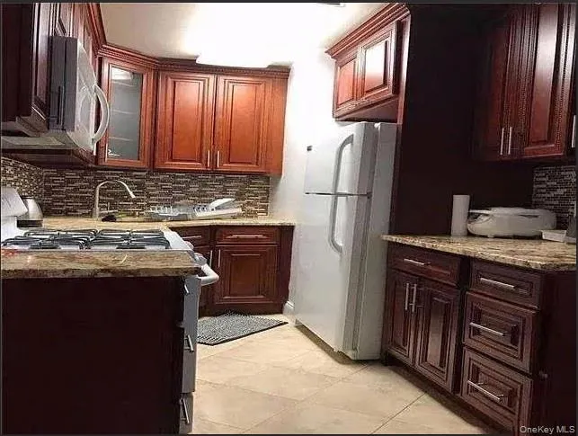 Kitchen with stainless steel appliances, glass insert cabinets, light stone counters, and decorative backsplash Kitchen with stainless steel appliances, glass insert cabinets, light stone counters, and decorative backsplash