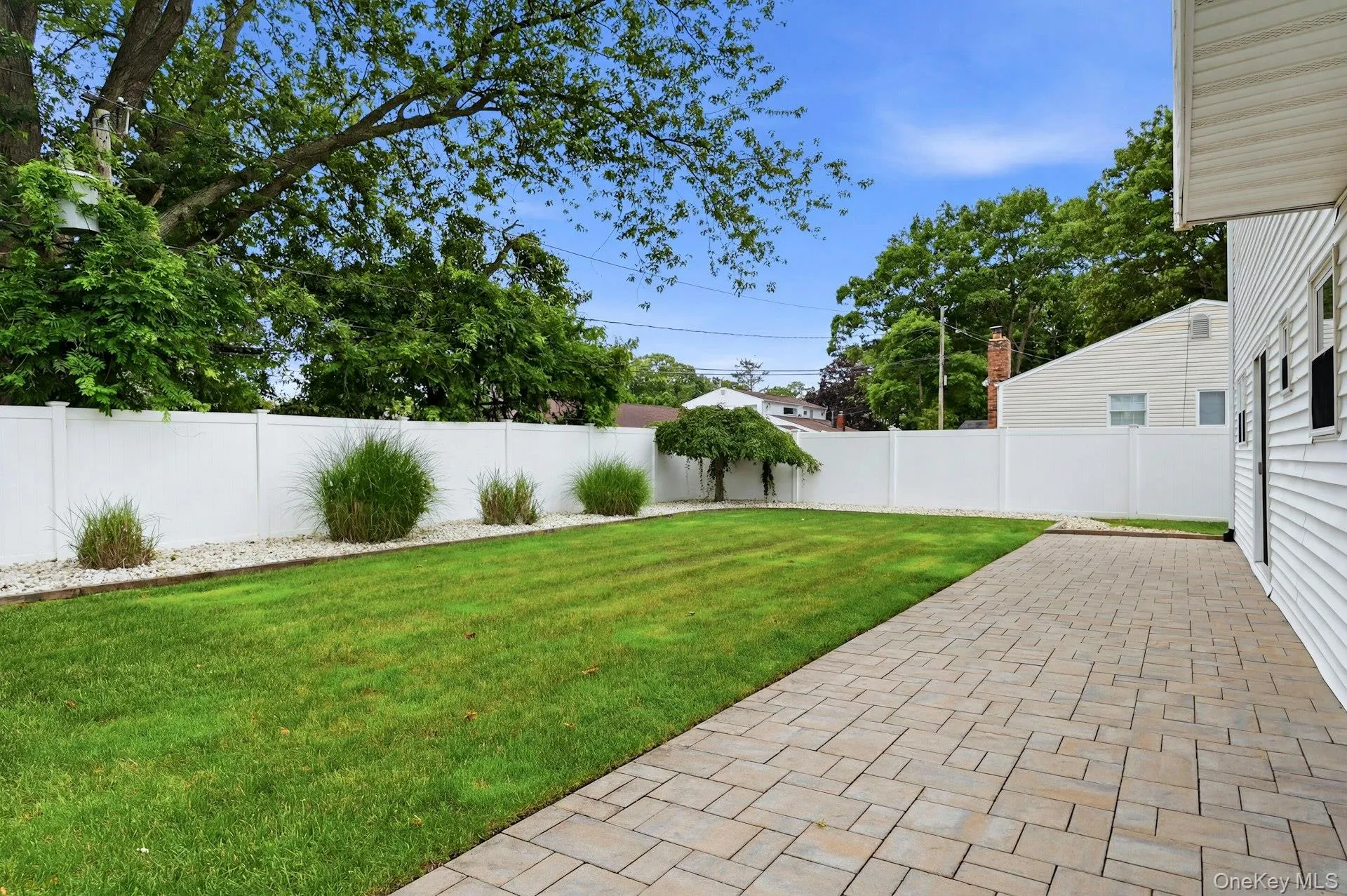 Expansive backyard featuring a paver patio, a lush lawn, and a white privacy fence Expansive backyard featuring a paver patio, a lush lawn, and a white privacy fence
