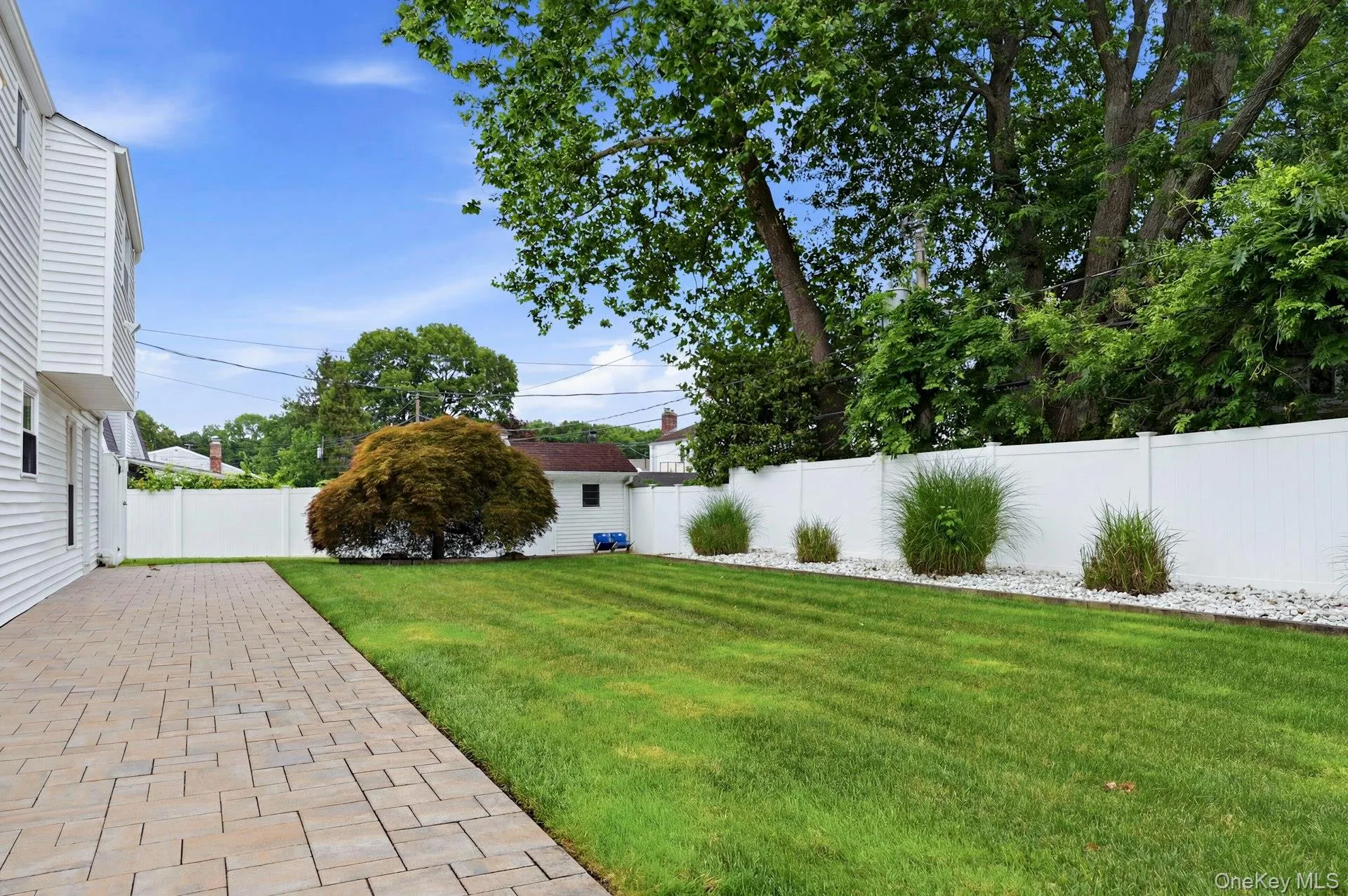 Expansive backyard featuring a paver patio, manicured lawn, white privacy fence, and mature landscaping Expansive backyard featuring a paver patio, manicured lawn, white privacy fence, and mature landscaping