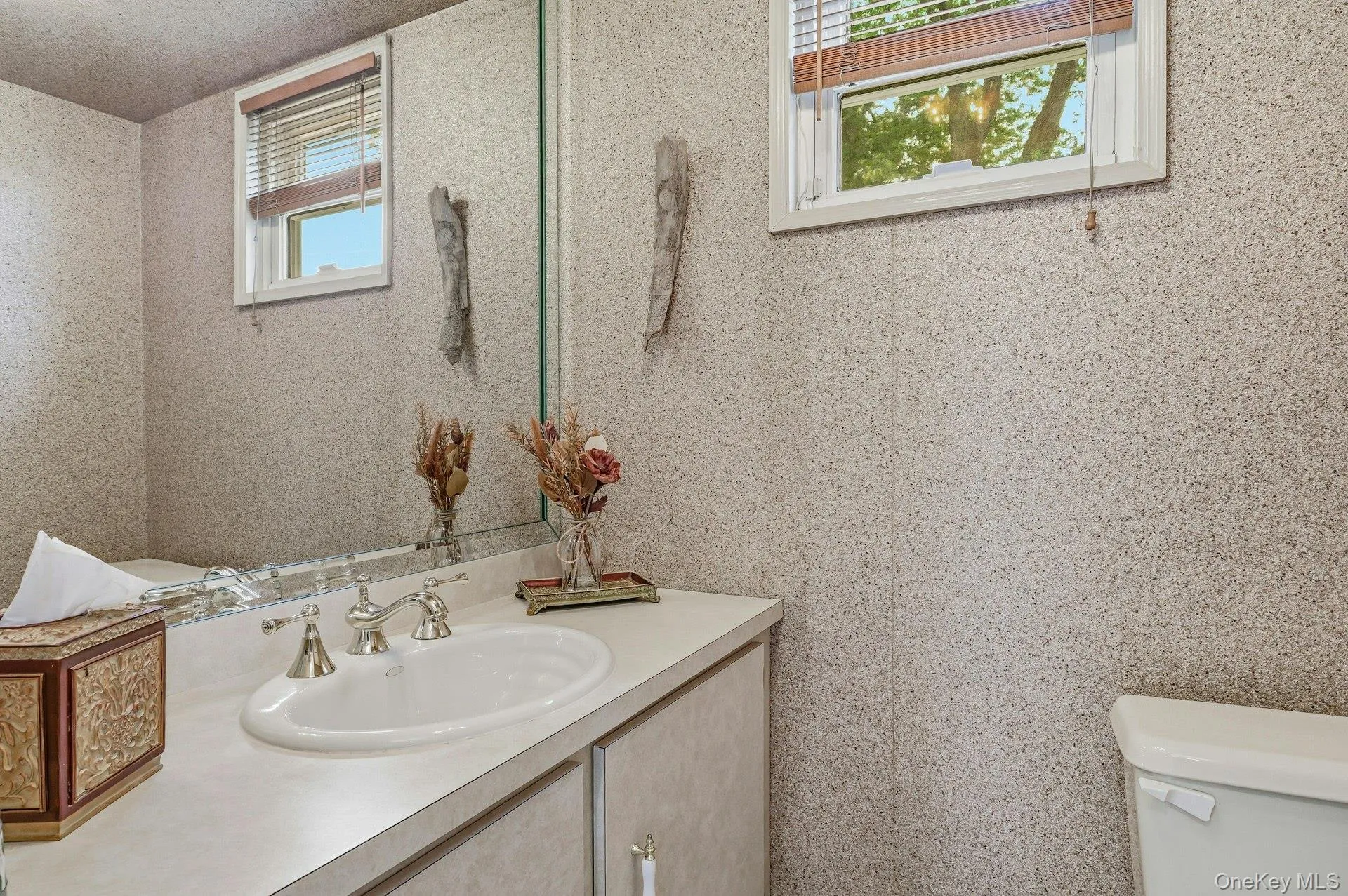 Bathroom vanity featuring an integrated sink with a chrome faucet, a large wall-mounted mirror, and a window with wood-finish blinds Bathroom vanity featuring an integrated sink with a chrome faucet, a large wall-mounted mirror, and a window with wood-finish blinds