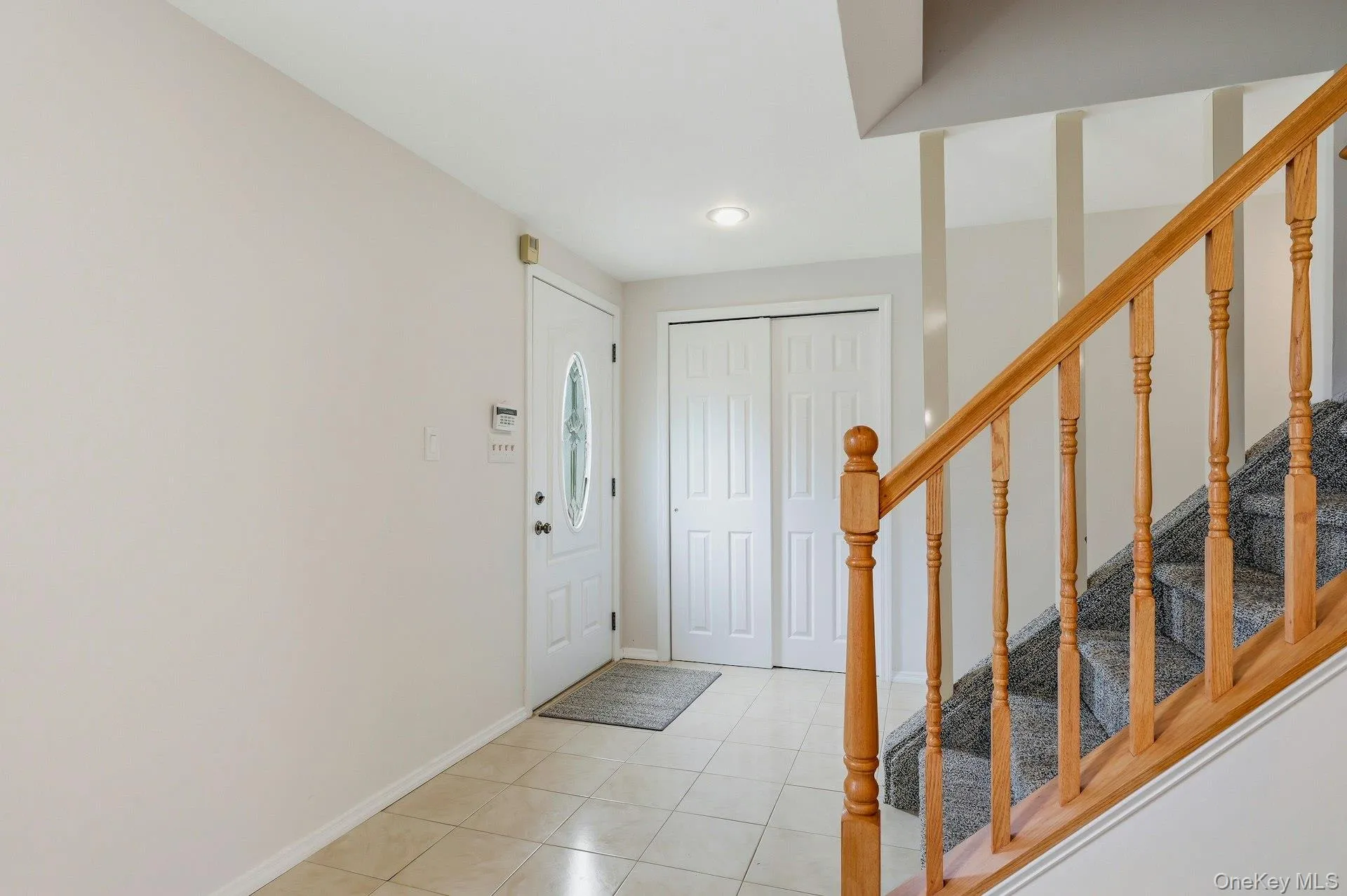 Entry foyer featuring neutral tile flooring, a white entry door with an oval-shaped decorative glass insert, and a built-in recessed light fixture Entry foyer featuring neutral tile flooring, a white entry door with an oval-shaped decorative glass insert, and a built-in recessed light fixture