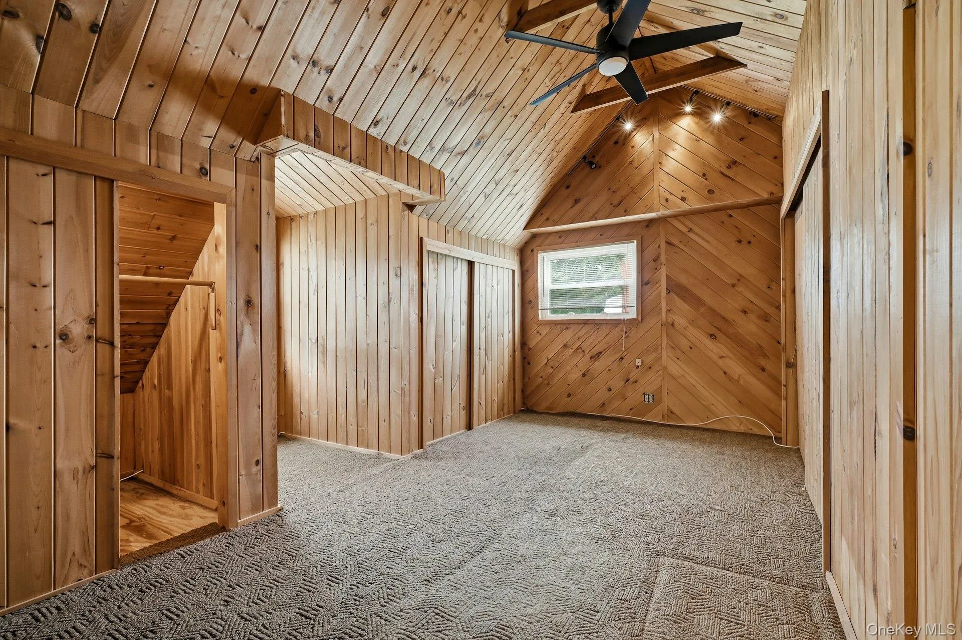 Vaulted wood-paneled room featuring patterned carpet flooring, a window, track lighting, and a ceiling fan Vaulted wood-paneled room featuring patterned carpet flooring, a window, track lighting, and a ceiling fan
