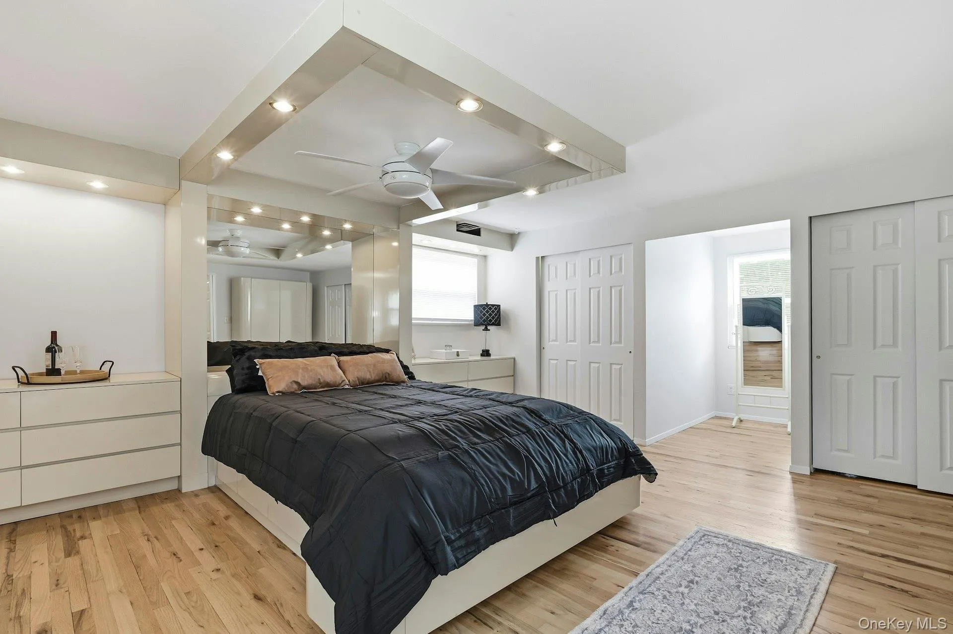 Wood-finish flooring throughout, featuring a recessed ceiling with integrated lighting and a ceiling fan Wood-finish flooring throughout, featuring a recessed ceiling with integrated lighting and a ceiling fan