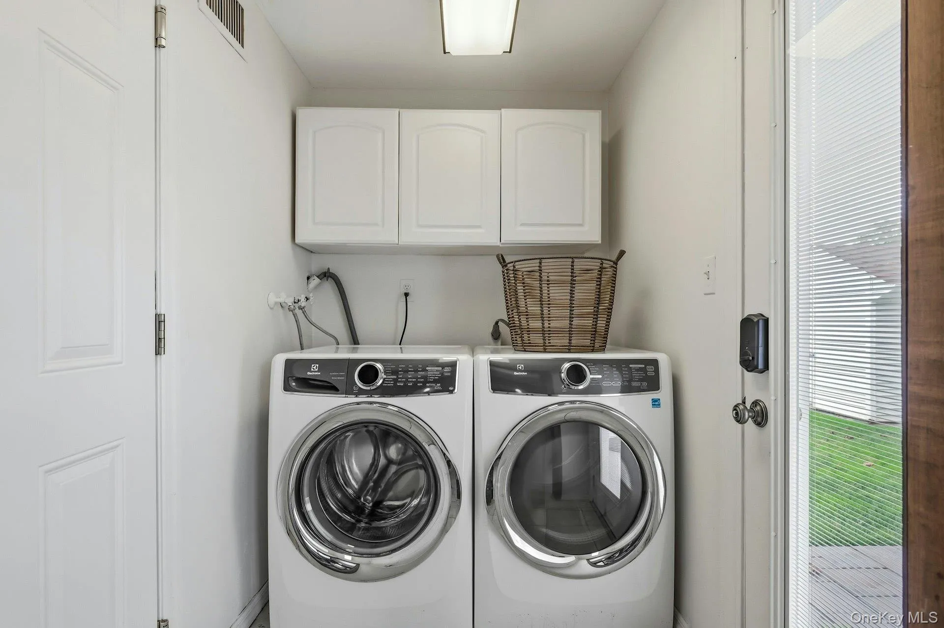 Dedicated laundry area featuring front-loading washer and dryer, upper cabinetry for storage, and a white paneled door Dedicated laundry area featuring front-loading washer and dryer, upper cabinetry for storage, and a white paneled door