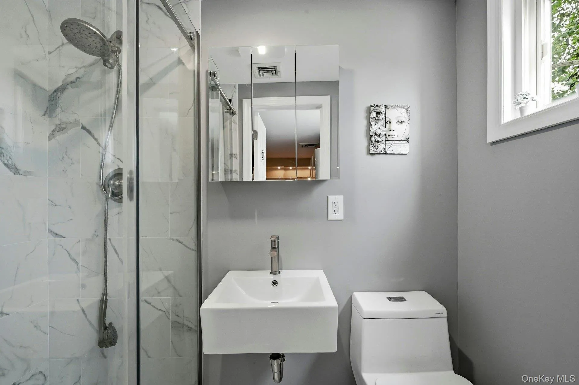 Sleek bathroom featuring a glass-enclosed shower with white marble-look tile, a wall-mounted rectangular sink, and a mirrored medicine cabinet Sleek bathroom featuring a glass-enclosed shower with white marble-look tile, a wall-mounted rectangular sink, and a mirrored medicine cabinet