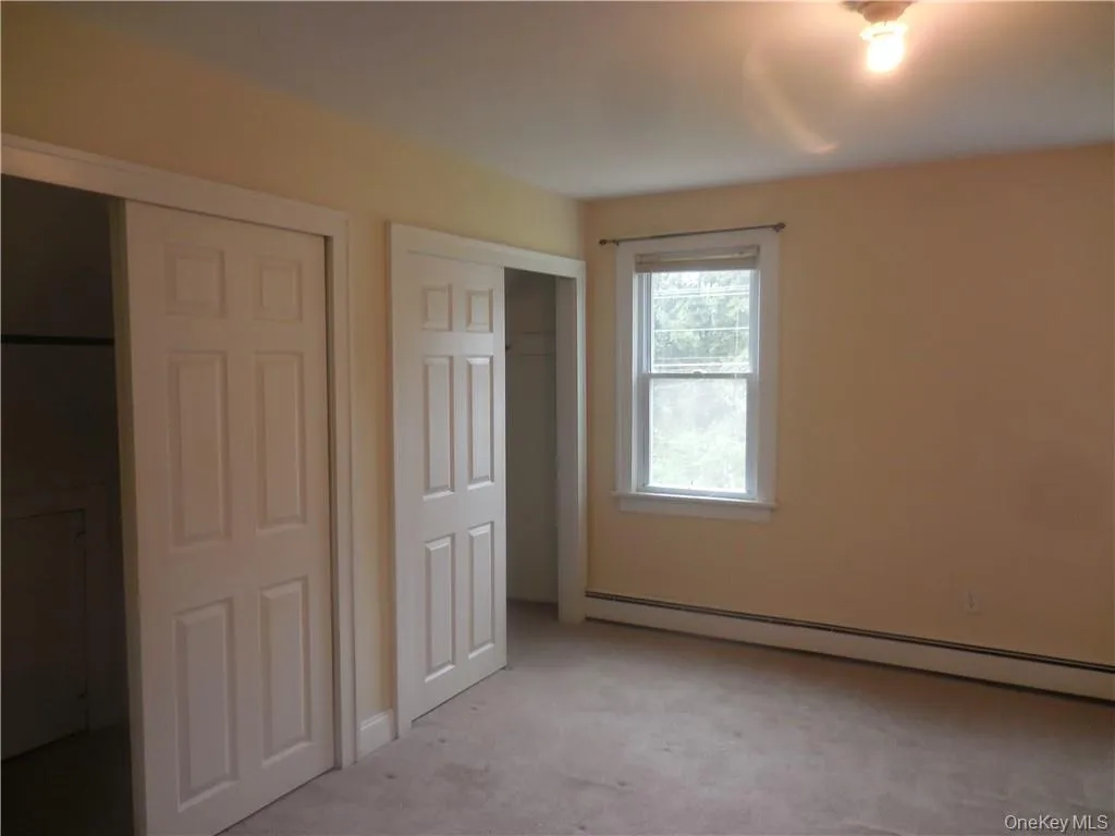 Unfurnished bedroom with a baseboard radiator and light carpet Unfurnished bedroom with a baseboard radiator and light carpet