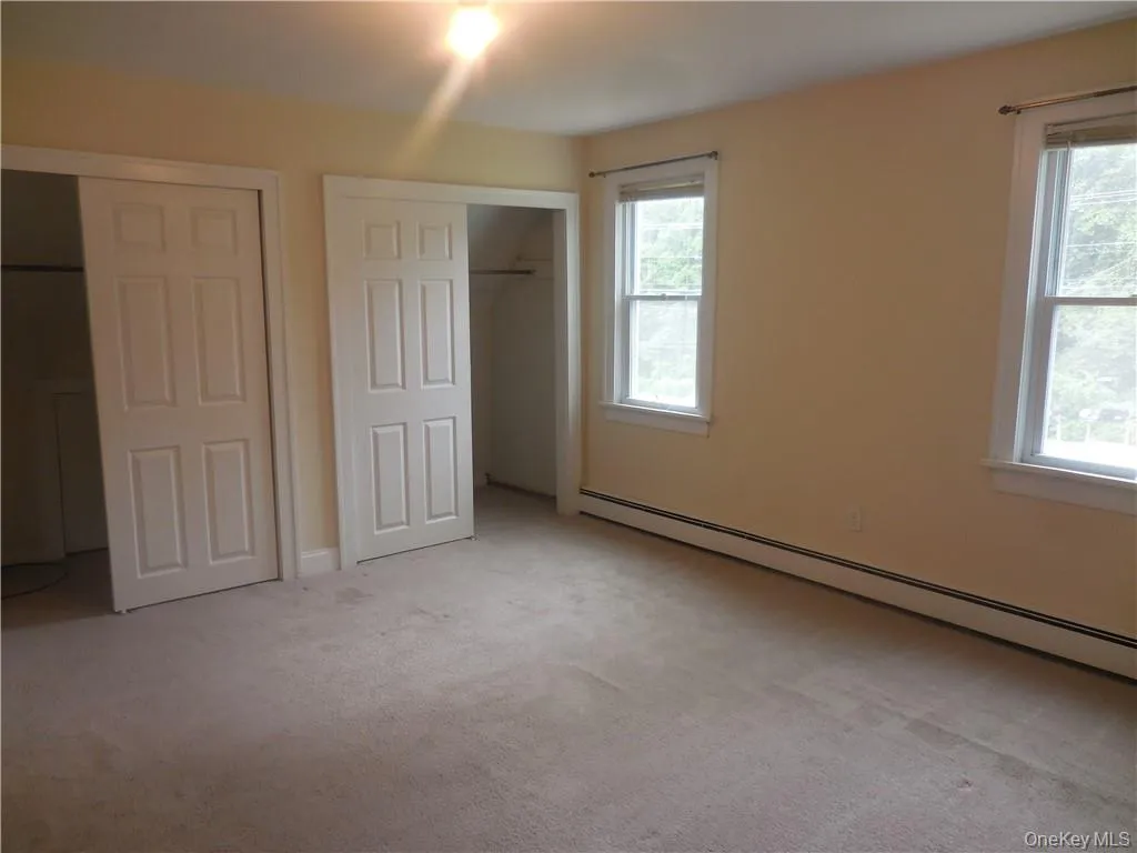 Unfurnished bedroom with light colored carpet and a baseboard radiator Unfurnished bedroom with light colored carpet and a baseboard radiator
