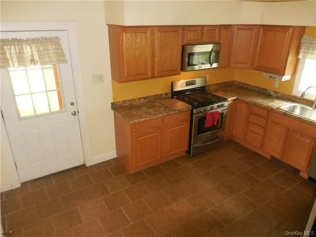 Kitchen featuring sink, stainless steel appliances, a wealth of natural light, and dark tile patterned flooring Kitchen featuring sink, stainless steel appliances, a wealth of natural light, and dark tile patterned flooring