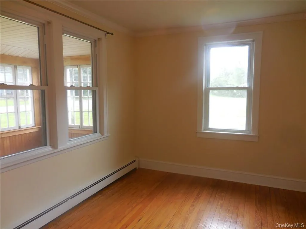 Empty room with crown molding, baseboard heating, and light hardwood / wood-style floors Empty room with crown molding, baseboard heating, and light hardwood / wood-style floors