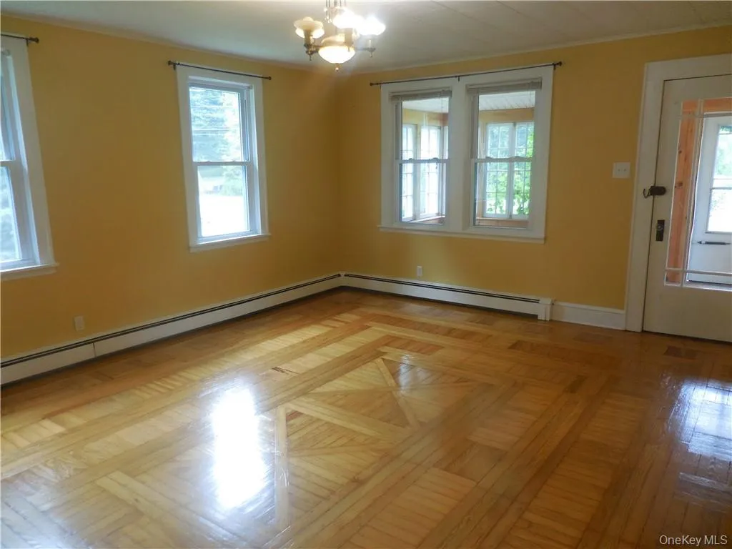 Empty room featuring a chandelier, a healthy amount of sunlight, baseboard heating, and light parquet floors Empty room featuring a chandelier, a healthy amount of sunlight, baseboard heating, and light parquet floors