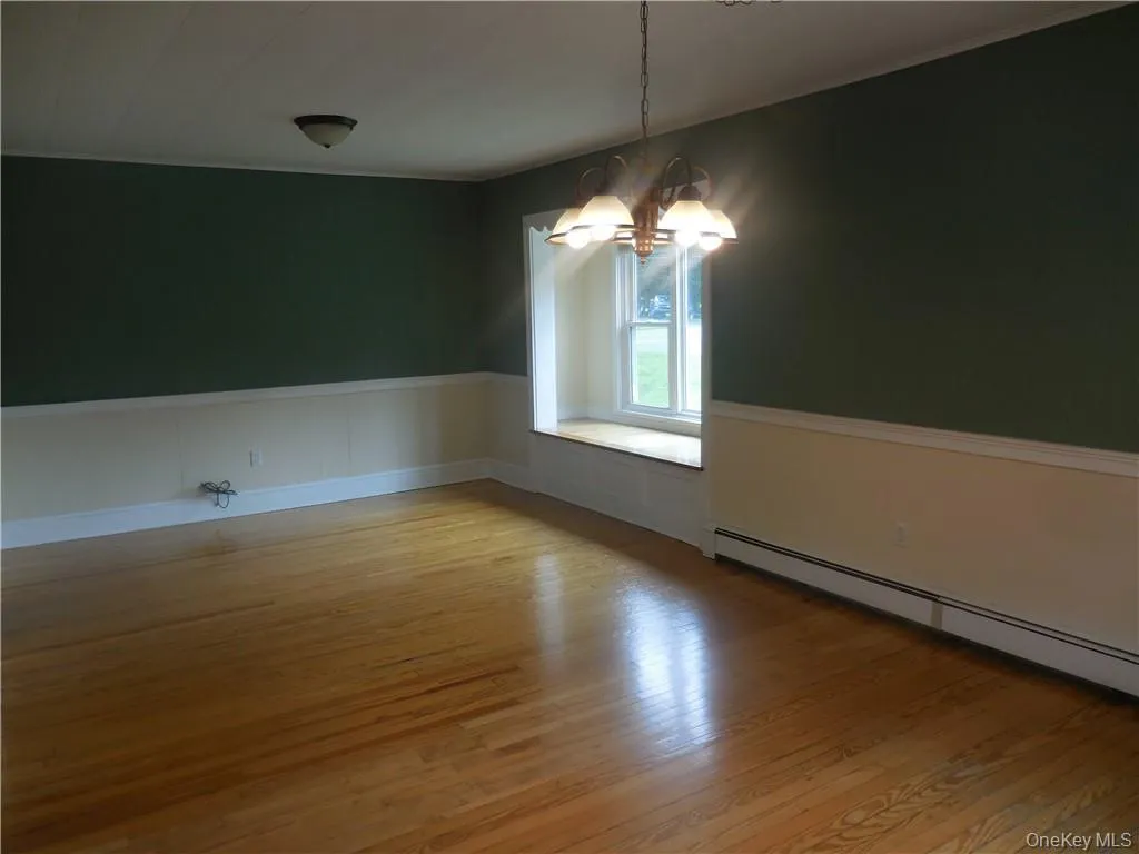 Unfurnished room featuring hardwood / wood-style floors, a baseboard radiator, a notable chandelier, and lofted ceiling Unfurnished room featuring hardwood / wood-style floors, a baseboard radiator, a notable chandelier, and lofted ceiling