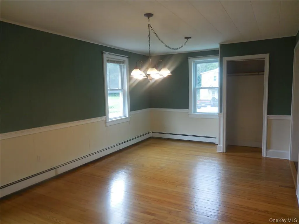Unfurnished dining area with light hardwood / wood-style flooring, a baseboard radiator, and an inviting chandelier Unfurnished dining area with light hardwood / wood-style flooring, a baseboard radiator, and an inviting chandelier