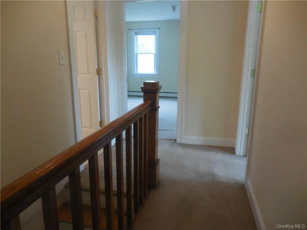 Corridor featuring a baseboard heating unit and light carpet Corridor featuring a baseboard heating unit and light carpet
