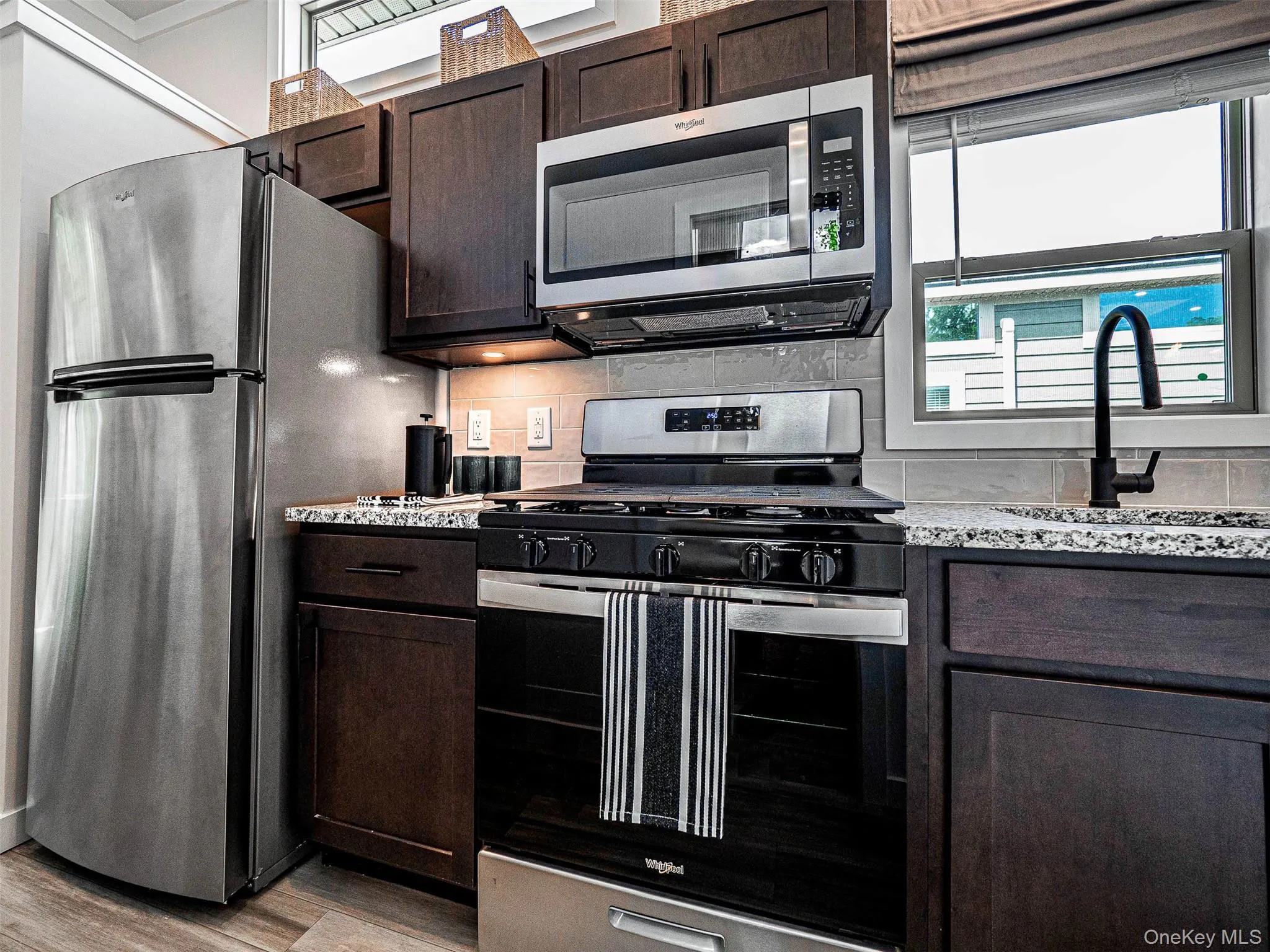 Kitchen featuring appliances with stainless steel finishes, dark brown cabinetry, decorative backsplash, and light wood-type flooring Kitchen featuring appliances with stainless steel finishes, dark brown cabinetry, decorative backsplash, and light wood-type flooring
