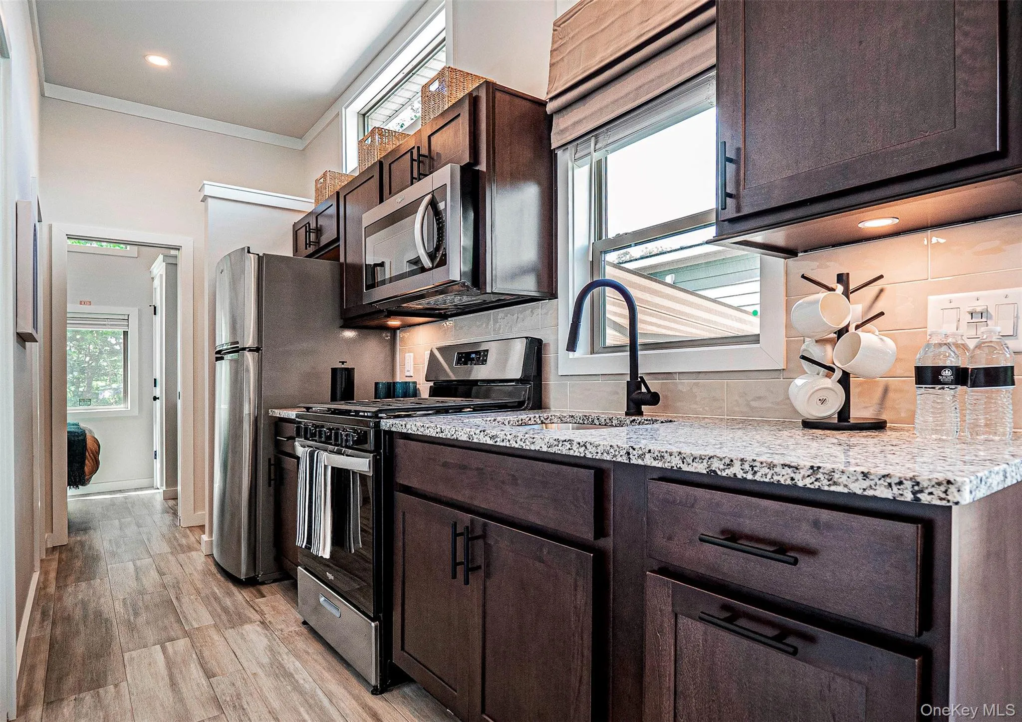 Kitchen featuring stainless steel appliances, dark brown cabinets, plenty of natural light, ornamental molding, and light wood-type flooring Kitchen featuring stainless steel appliances, dark brown cabinets, plenty of natural light, ornamental molding, and light wood-type flooring