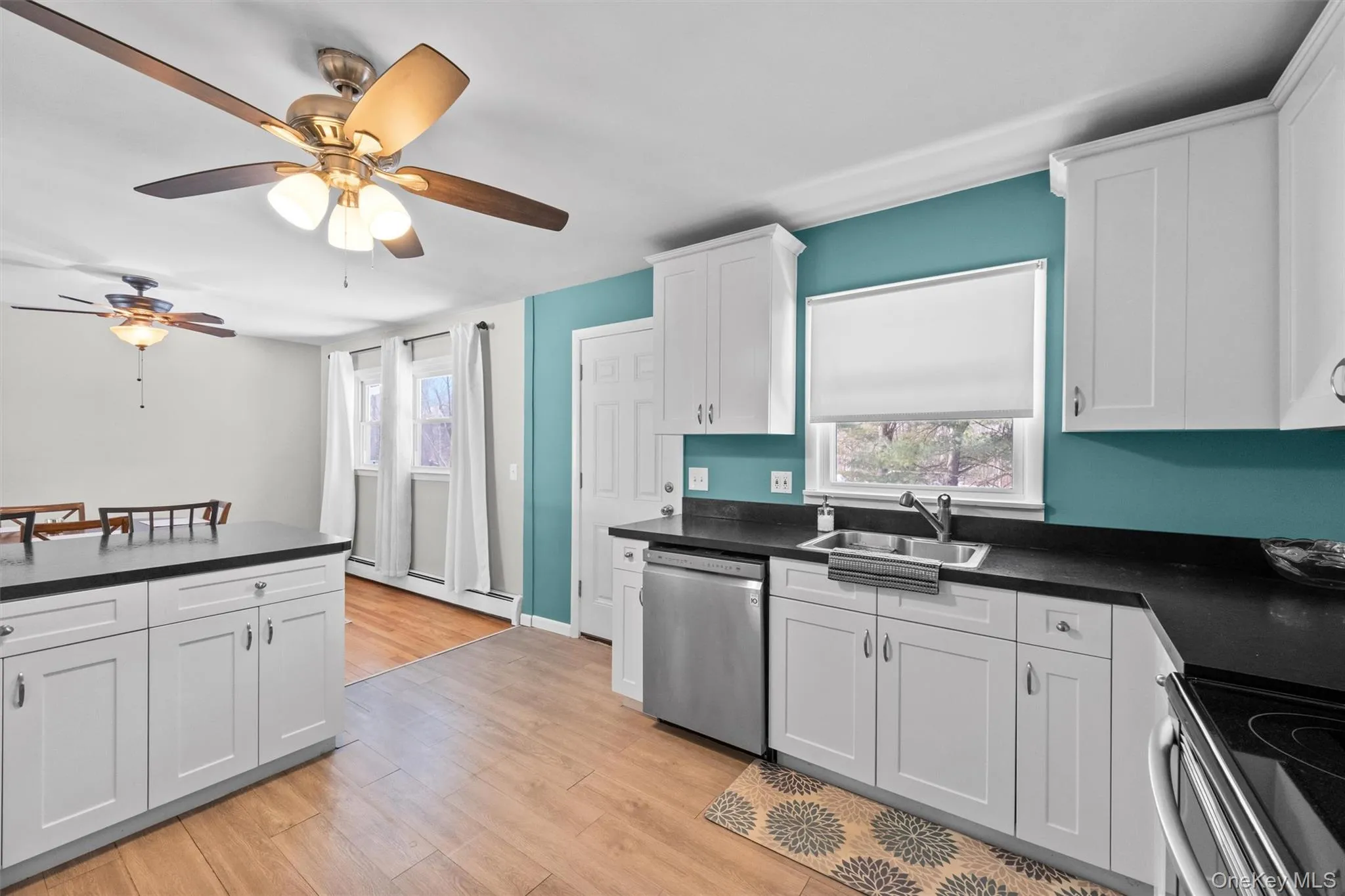 Kitchen with a sink, white cabinetry, light wood-type flooring, dishwasher, and dark countertops Kitchen with a sink, white cabinetry, light wood-type flooring, dishwasher, and dark countertops